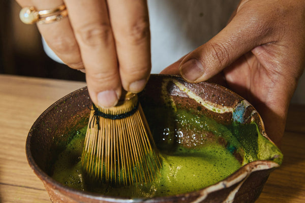 Hands whisking matcha in a rustic ceramic bowl, morning light