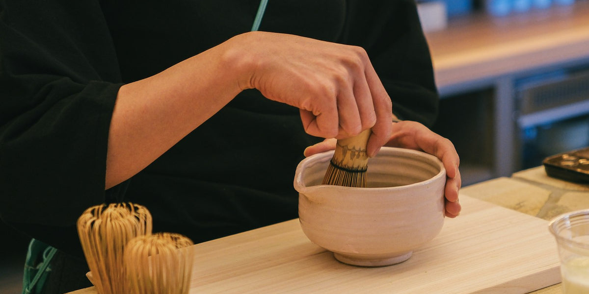 Matcha being whisked in a ceramic bowl with bamboo chasen — neutral kitchen light