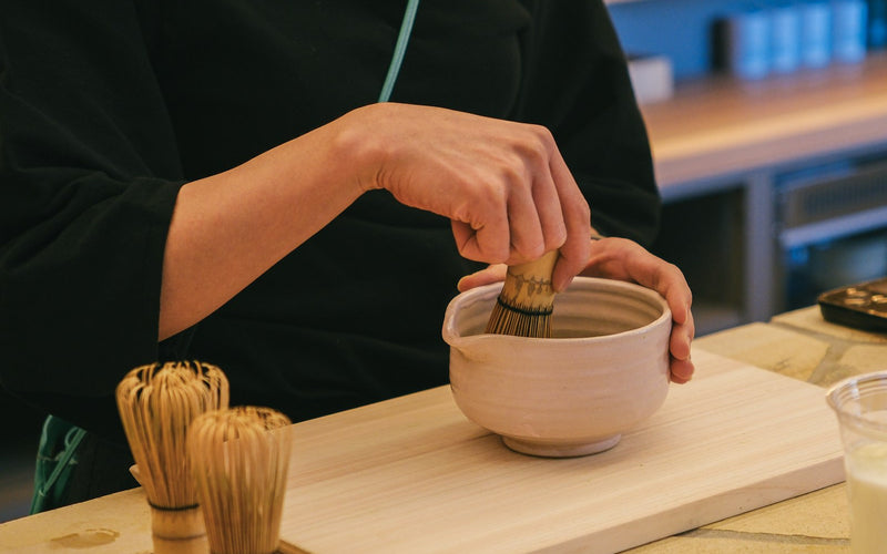 Matcha being whisked in a ceramic bowl with bamboo chasen — neutral kitchen light