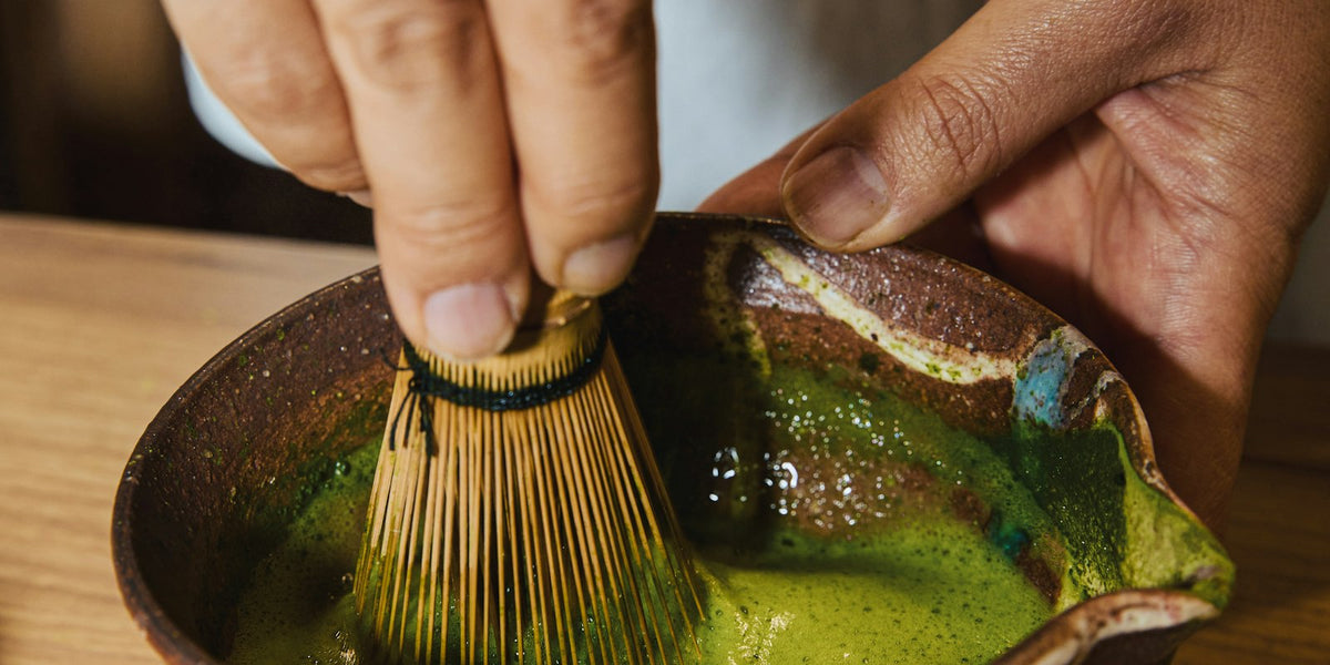 Hands whisking matcha in a rustic ceramic bowl, morning light