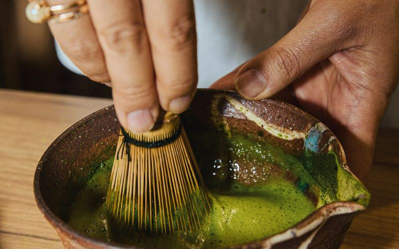 Hands whisking matcha in a rustic ceramic bowl, morning light