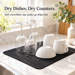 Black dish drying mat on a marble kitchen counter with glasses, mugs and a bowl drying on it