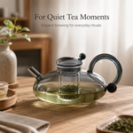 Ash-grey glass teapot brewing green tea on a wood table for quiet tea moments