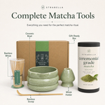 Ceremonial matcha powder and bamboo accessories arranged on linen tea mat with green chawan