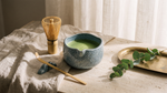 Matcha whisk set styled on a travertine counter with linen and brass tray, blue ceramic chawan with whisked matcha