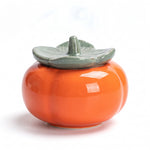 ceramic tea caddy — persimmon jar with sage-green leaf lid on white