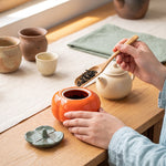 ceramic tea caddy — scooping loose leaf tea into the open persimmon jar