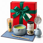 Christmas Matcha Gift Box, Blue: red gift box with a green satin bow standing behind the blue 7-piece matcha whisk set and Ceremonial Matcha tin
