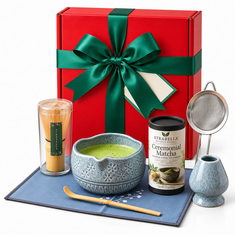 Christmas Matcha Gift Box, Blue: red gift box with a green satin bow standing behind the blue 7-piece matcha whisk set and Ceremonial Matcha tin