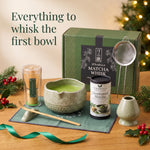 Green 7-piece matcha whisk set with bamboo chasen, ceramic chawan, holder, scoop, sifter and mat, next to the 54 g ceremonial matcha tin