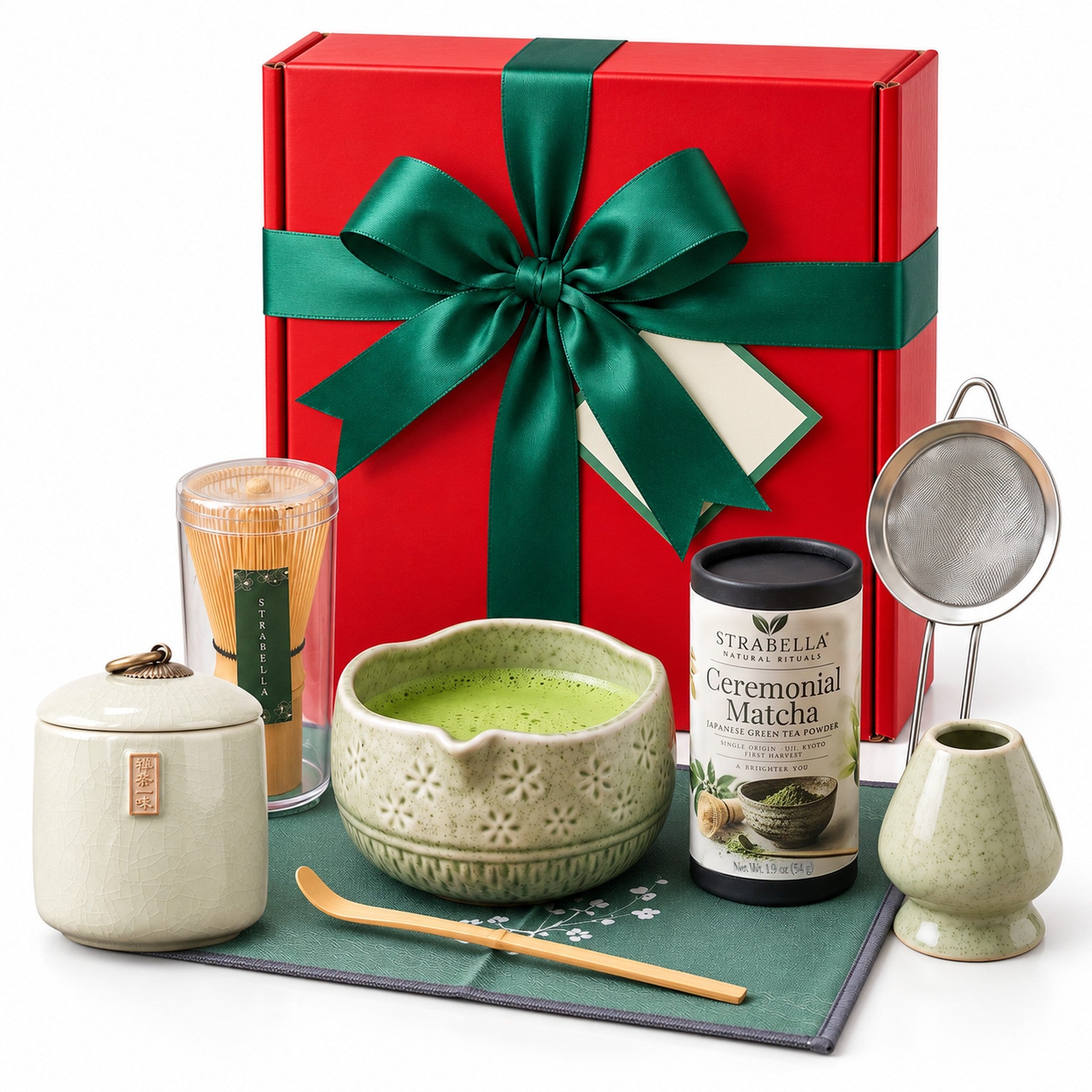 Christmas Matcha Gift Box Deluxe, Green: red gift box with a green satin bow standing behind the green 7-piece matcha whisk set, Ceremonial Matcha tin and cream Ru Kiln tea caddy