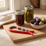 Jar opener — red opener on a wooden board beside jars of jam and pickles