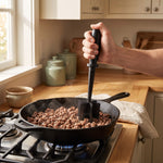 Meat chopper in use — hand pressing the chopper into ground beef browning in a cast-iron skillet